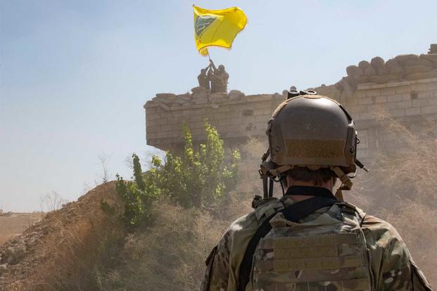 A U.S. Soldier oversees members of the Syrian Democratic Forces as they demolish a YPG fortification and raise a Tal Abyad Military Council flag over the outpost as part of the security mechanism zone agreement, Sept. 21, 2019. (U.S. Army/Staff Sgt. Andrew Goedl)