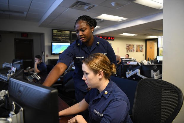 Petty Officer 1st Class Lecia Mauge-Chan (standing) and Petty Officer 2nd Class Amanda Lewis (seated) stand watch as operations specialists in the command center of Coast Guard Sector Hampton Roads in Portsmouth, Virginia.