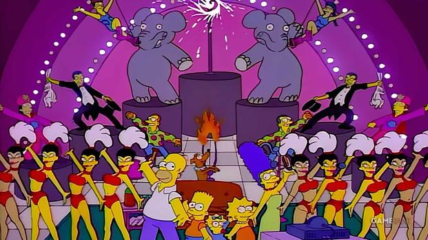 The Simpsons stand on a giant Las Vegas stage with their family sofa and a line of showgirls.