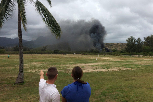 In this May 17, 2015 photo, a man and woman look toward smoke rising from a Marine Corps Osprey aircraft after making a hard landing on Bellows Air Force Station near Waimanalo, Hawaii. (Zane Dulin via AP)
