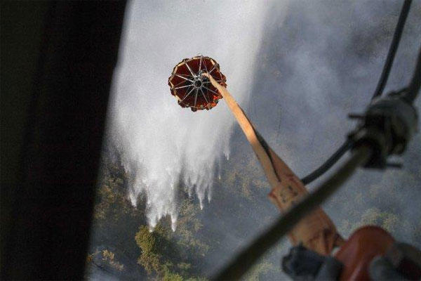 A Bambi Bucket, hanging from an Alaska Army National Guard Black Hawk helicopter, releases more than 700 gallons of water onto the Stetson Creek Fire near Cooper Landing, Alaska, June 17, 2015.(U.S. Army National Guard/Sgt. Balinda ONeal)