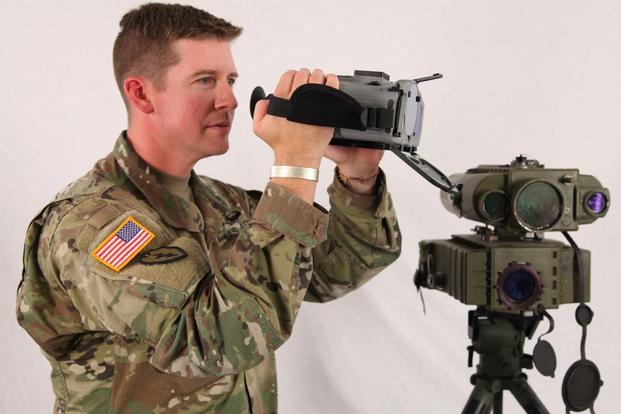 Maj. Robert J. Heatherly, holds a new Joint Effects Targeting System next to the current, tripod mounted Lightweight Laser Designator Rangefinder. (Army Photo)