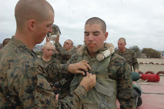 FILE -- Recruit Andrew O’Shoughnessy, left, Platoon 2106, Company E, 2nd Recruit Training Battalion, snaps the buttons down on the flak jacket of Eric Rueseler. (Marine Corps Photo/ Lance Cpl. Katalynn Thomas)