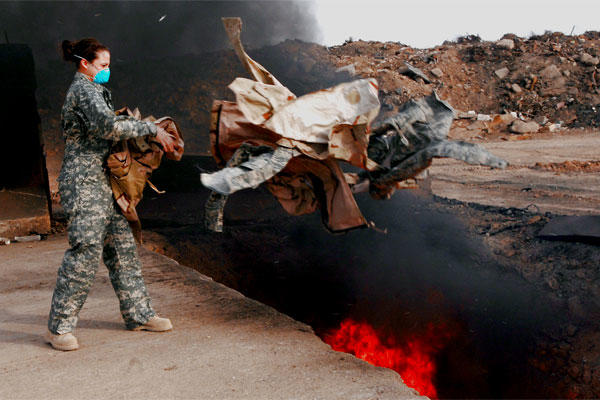 An airman tosses uniform items into a burn pit at Balad Air Base, Iraq, on March 10, 2008. (US Air Force photo/Julianne Showalter)