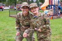 A mom and son pose on a playground in matching military camouflage uniforms.