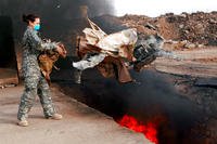 A senior airman tosses unserviceable uniform items into a burn pit at Balad Air Base, Iraq, in March 2008. (US Air Force photo/Julianne Showalter)