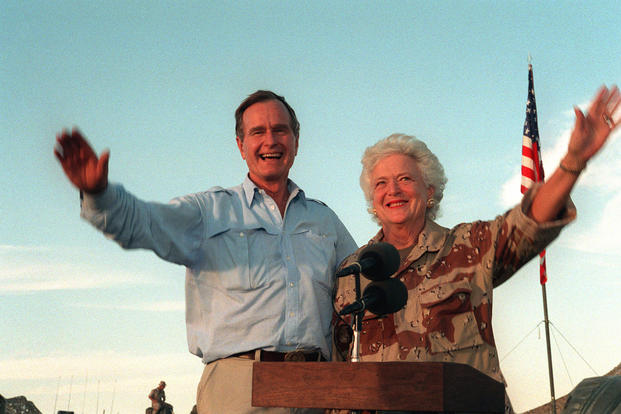 U.S. President George H.W. Bush and first lady Barbara Bush wave as they stand in the back of a vehicle during a visit to a desert encampment in Saudi Arabia, Nov. 22, 1990. The former president and his wife were paying Thanksgiving Day visits to U.S. troops in Saudi Arabia for Operation Desert Shield. (U.S. Navy photo/Ed Bailey)