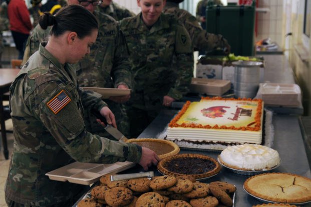 A soldier cuts into a pumpkin pie during a Thanksgiving meal.
