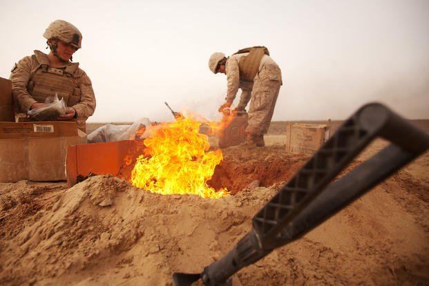 Marines burn trash in a burn pit.