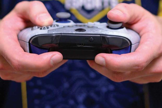 A Navy esports team player holds a game controller.
