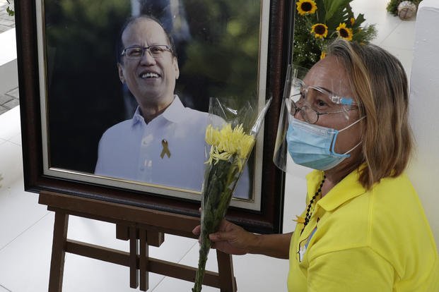 A supporter sits beside a picture of former Philippine President Benigno Aquino III beside his tomb.