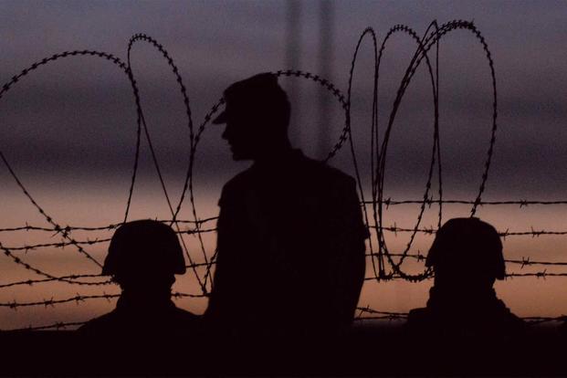 A group of soldiers are silhouetted against the evening sky