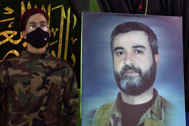 A Hezbollah fighter stands next to a picture of Ali Atwa