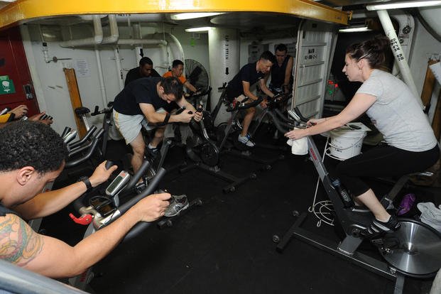 Sailors participate in spin class aboard an aircraft carrier.