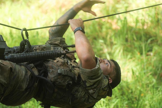 A soldier climbs across a rope bridge.
