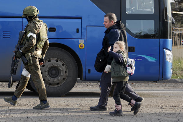 A man and a girl walk to a bus escorting by a serviceman of Russian Army in Mariupol.