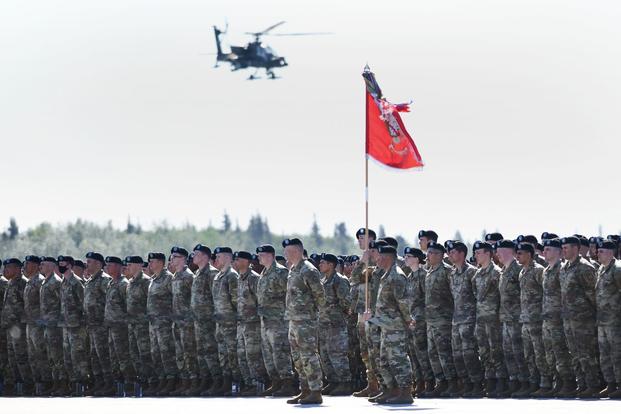 Soldiers stand in formation as an AH-64 Apache helicopter flies overhead in Alaska. 
