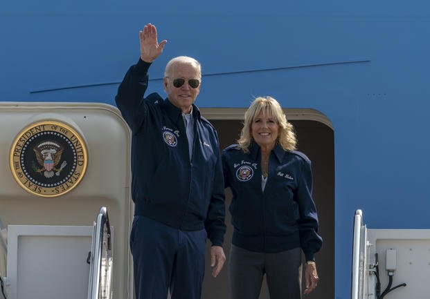 President Joe Biden waves as first lady Jill Biden watches standing at the top of the steps of Air Force One