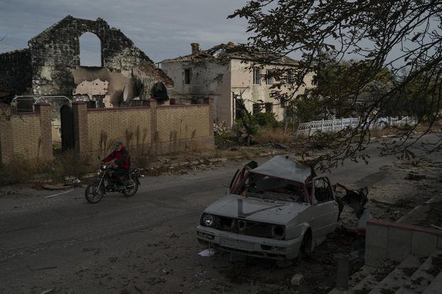 A man drives his motorcycle past a destroyed car in the retaken village of Velyka Oleksandrivka