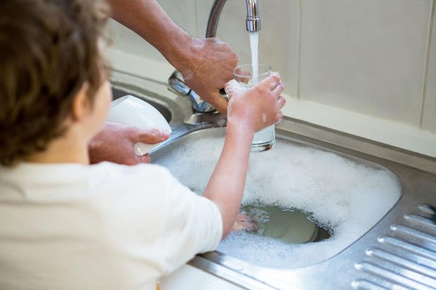 A parent and child filling water glass from kitchen sink