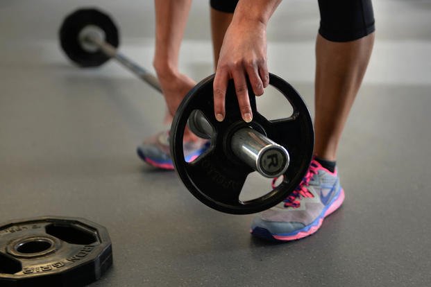 A beginner athlete in the newly offered tactical fitness class, OnRamp, adds a 10-pound weight to a barbell at Minot Air Force Base, N.D.