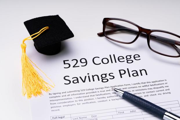 A 529 college savings plan, glasses, a pen, and a tiny graduation cap are arranged on a surface
