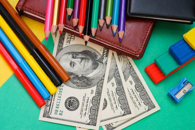 Colored pencils and markers are arranged on a desk with wallets and $100 bills