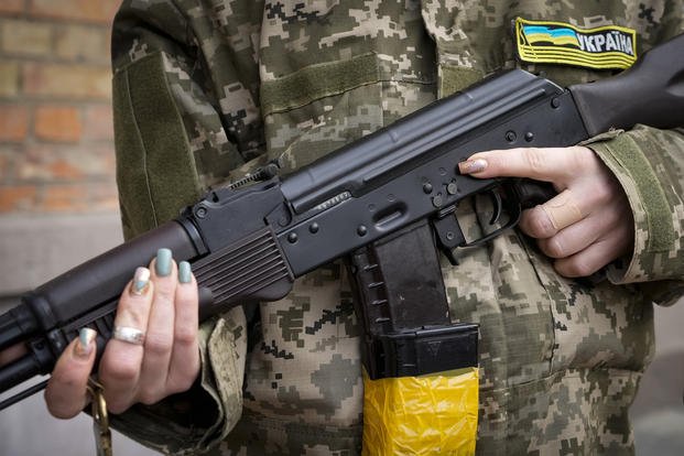 An armed civil defense woman holds a Kalashnikov assault rifle while patrolling an empty street in Kyiv, Ukraine.