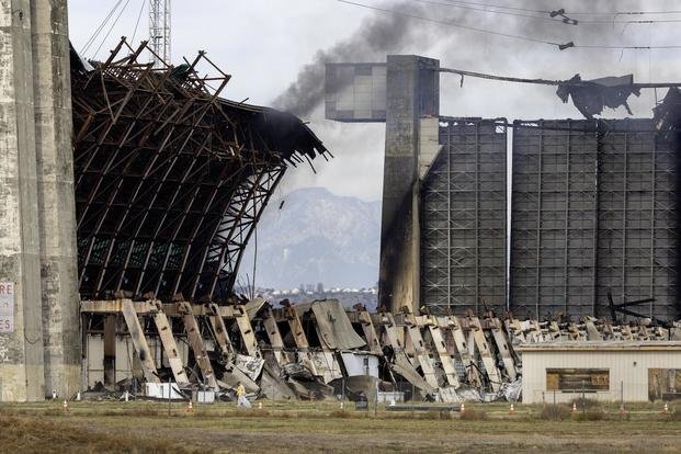 A disaster cleanup crew picks up potentially toxic debris around the still-burning, World War II-era blimp hangar at the former air base in Tustin, California.