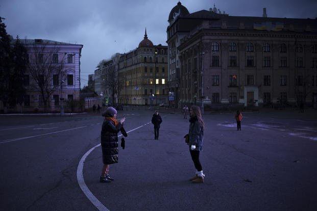 People walk and take photos on a street closed for cars at dusk in Kyiv