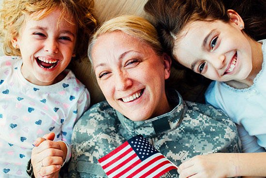 Military mom holding US flag with young daughters