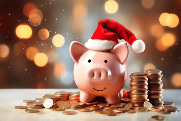 A piggy bank wearing a Santa hat smiles amid shiny coins and against a backdrop of twinkling lights.
