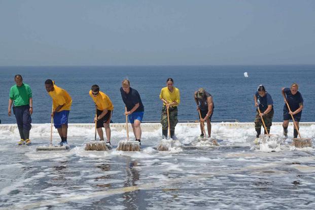 Navy sailors scrub a flight deck with aqueous film-forming foam