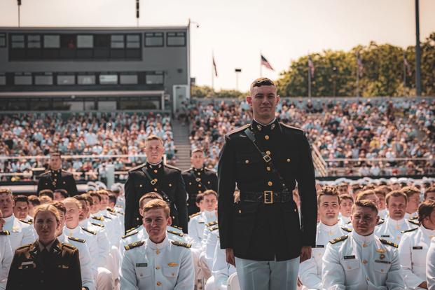 Amid white-jacketed military academy graduates, dark-jacketed graduates stand in recognition.