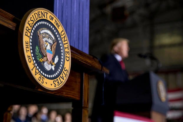 The presidential seal is visible as President Donald Trump, background, speaks