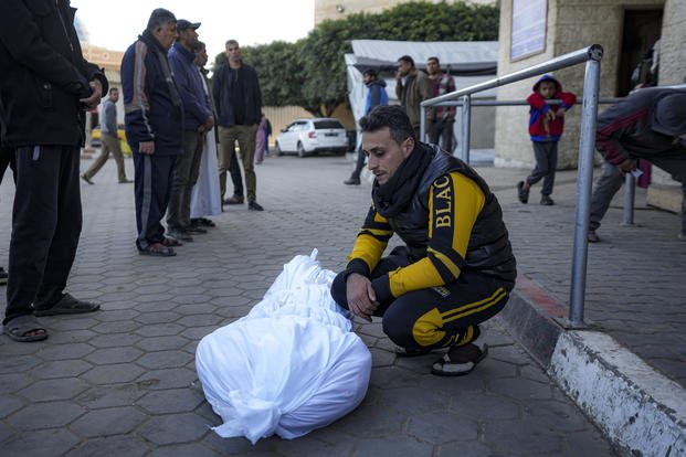 A man sits by the body of a Palestinian killed in the Israeli bombardment of the Gaza Strip at Al-Aqsa Hospital