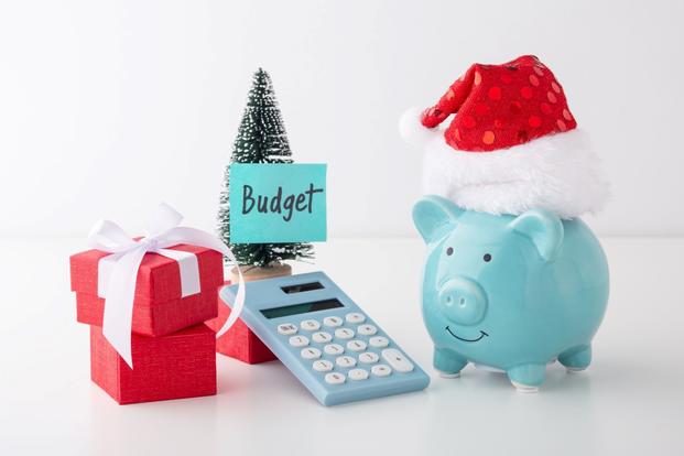 In tones of light blue and red, a piggy bank in a Santa cap, a calculator, gifts and a tree decoration make up an arrangement.