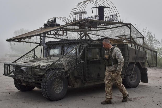 Ukrainian soldier passes by an armoured Hummer vehicle equipped with an anti-drone net