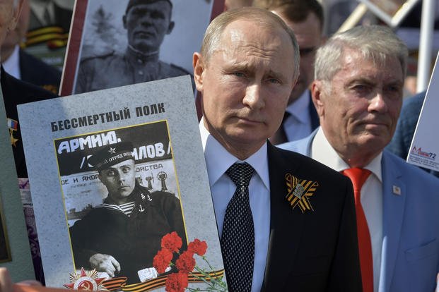 Russian President Vladimir Putin, center, holds a portrait of his father, also named Vladimir