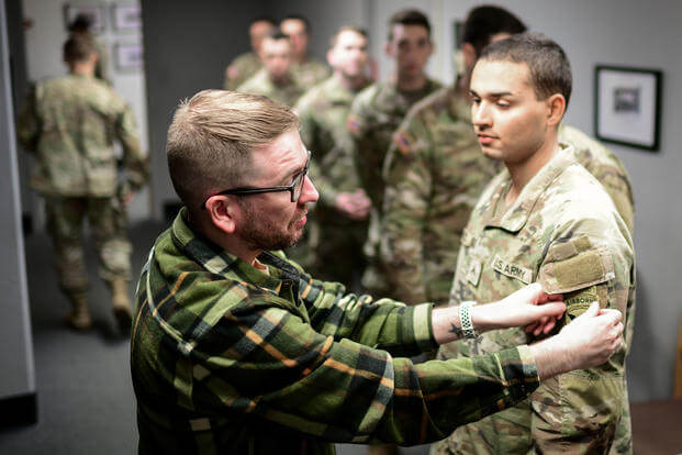 Civilian Airman Nicholas Holland, left, a photographer assigned to the 673d Air Base Wing Public Affairs, helps Army Private Juan Pacheco, a replacement in the 11th Airborne Division, adjust his uniform before having his official Individual Readiness Processing Program photograph taken at Joint Base Elmendorf-Richardson, Alaska, March 14, 2025. (Justin Connaher/U.S. Air Force)