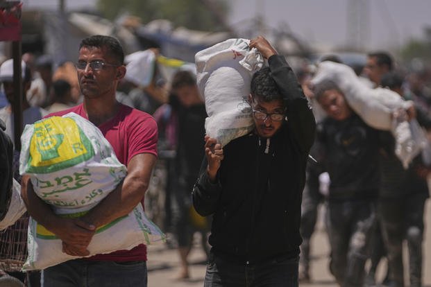 Palestinians carry bags containing food and humanitarian aid packages delivered by the Gaza Humanitarian Foundation