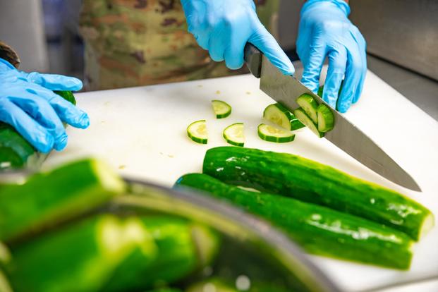 Culinary specialists from the Connecticut Army National Guard cut up cucumbers while preparing a meal inside a containerized kitchen at Fort Drum