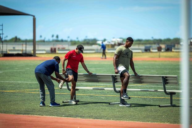 A coach shows two athletes how to stretch their legs.