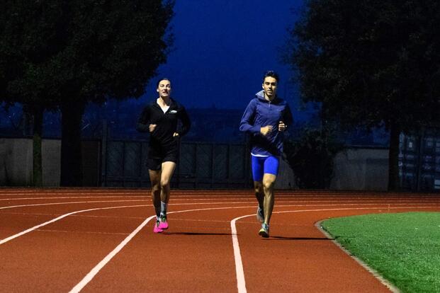 Two runners side by side on a track at night.