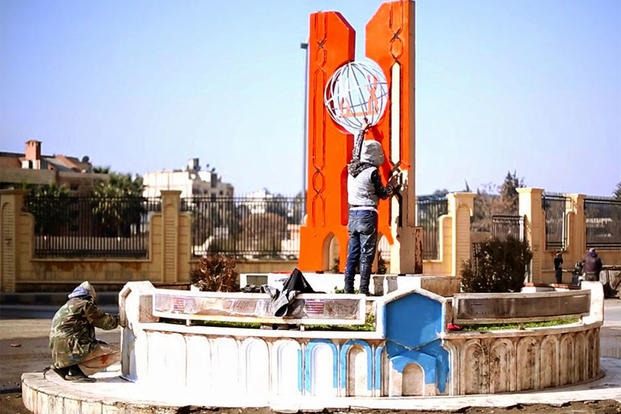 In this photo released on April 25, 2015, by a militant website, which has been verified and is consistent with other AP reporting, members of the Islamic State group, paint a decoration on a main square in Raqqa, Syria. (Militant website via AP)