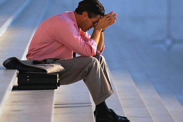 Depressed businessman sitting on stairs wearing a pink shirt.