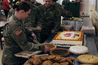 A soldier cuts into a pumpkin pie during a Thanksgiving meal.