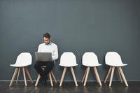 Shot of a young man using a laptop while waiting in line for a job interview