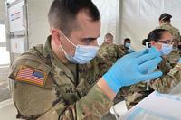 Soldiers fill syringes with COVID-19 vaccine.