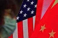 A woman wearing a face mask sits near a screen showing China and U.S. flags.